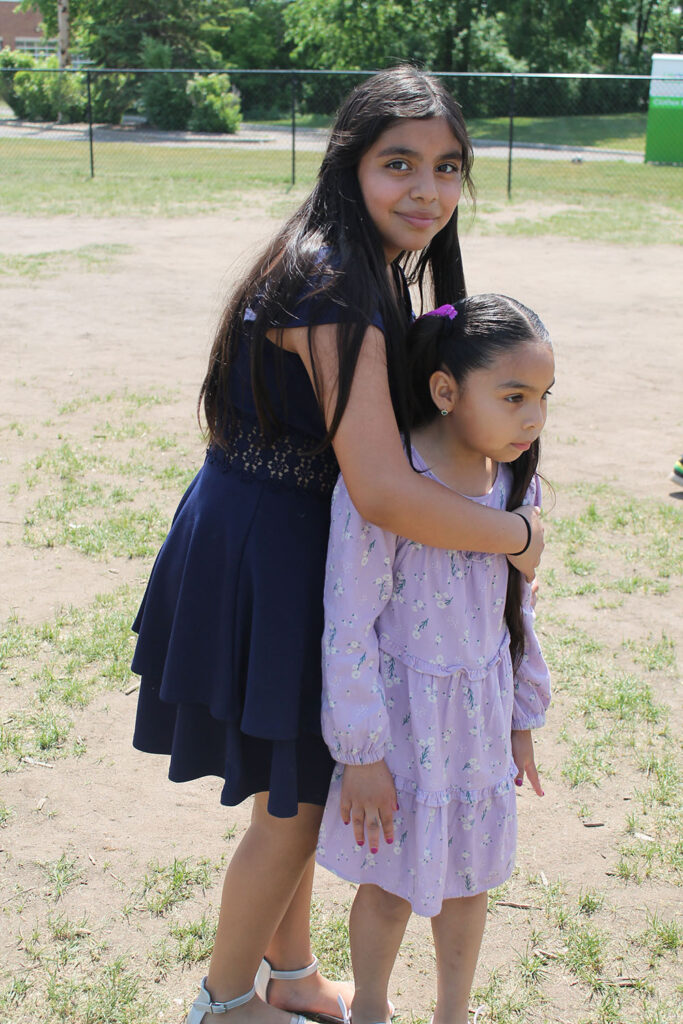 young 5 th grade girl standing with her arm around a Kindergarten girl