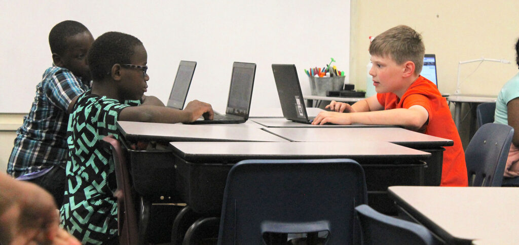 Three 4 th grade boys sitting at their desks looking at their school laptops