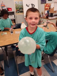 young boy in art class holding a slime bubble he made